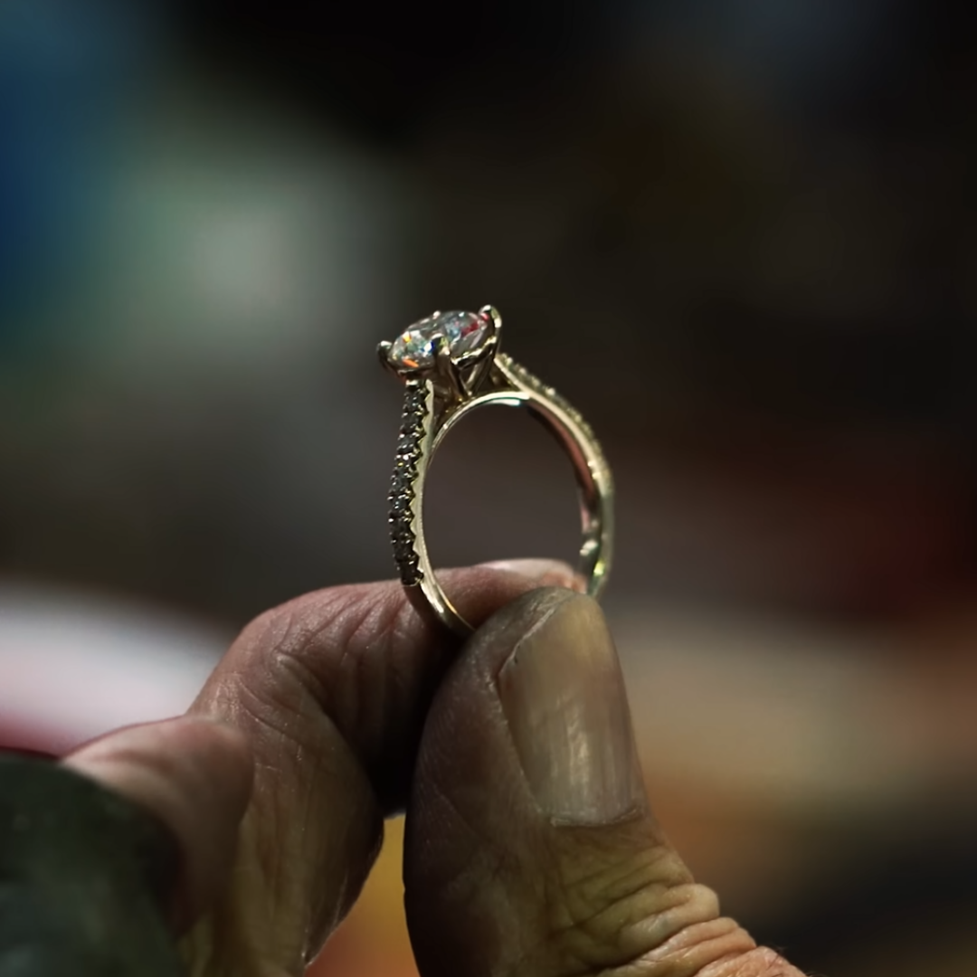 Close-up of a hand holding a diamond ring in a yellow gold setting