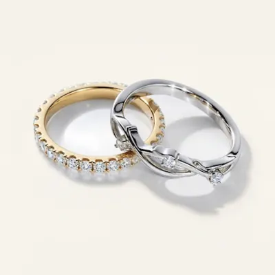 Three men’s wedding bands stacked together: a white gold band with pavé diamonds, a yellow gold hammered-texture band, and a plain polished yellow gold band, displayed on a cream background.