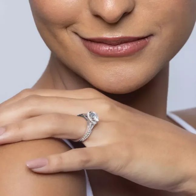 A close-up of Clarissa Split Shank Halo Engagement Ring on a woman's ring finger