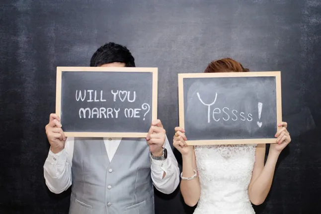 A bride and groom standing next to each other with chalkboards saying will you marry me? Yessss! Moissanite for engagement ring?