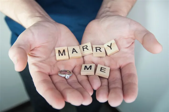 Marry me written in scrabble letters in a gent's hand with an engagement ring. 