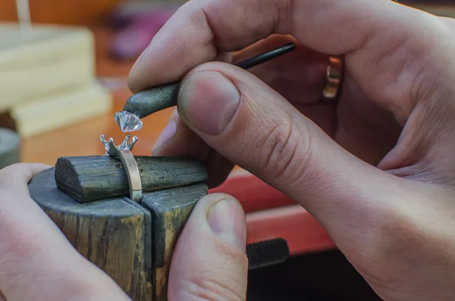 A jeweler setting a diamond into a yellow gold solitaire 4 prong mounting 