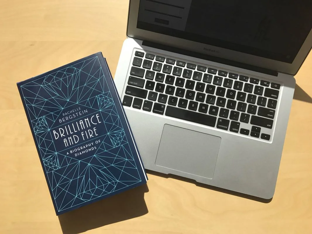 Flat lay image of an open laptop and the book 'Brilliance and Fire' on a tabletop