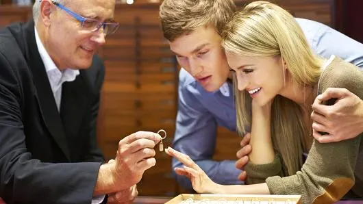 A jewelry salesperson showing a wedding band to a couple shopping together