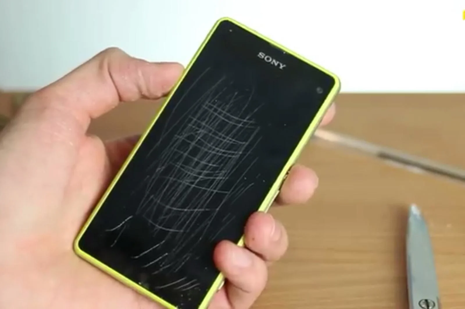 Close-up of a hand holding a smartphone with visible scratches on the screen