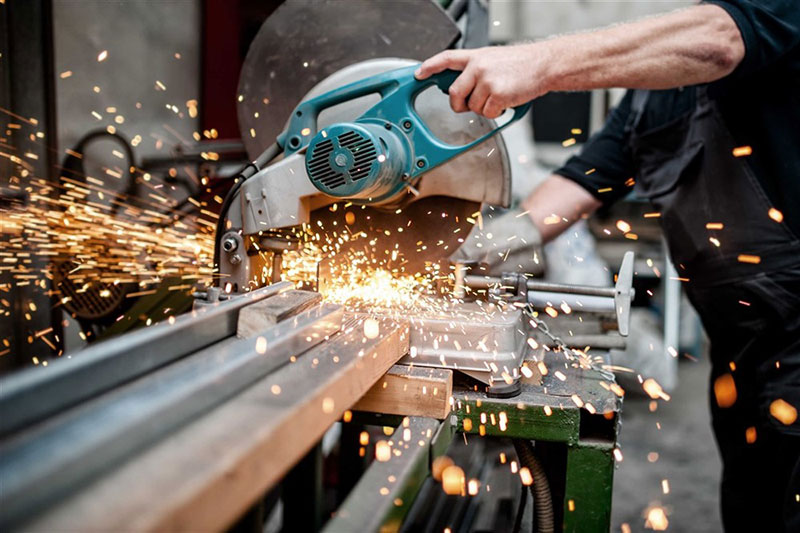 A power saw operated by a worker, cutting metal and creating bright sparks in a workshop setting