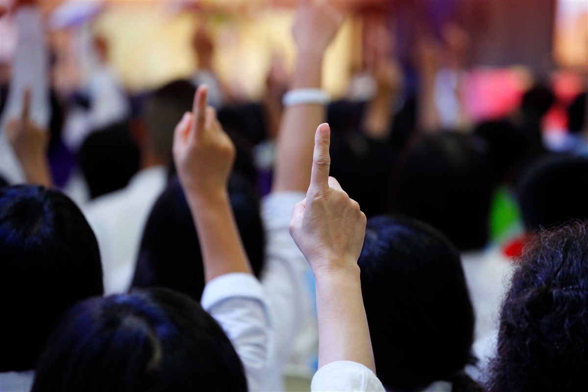 Bidders raising their hands with index fingers pointed upward at an auction