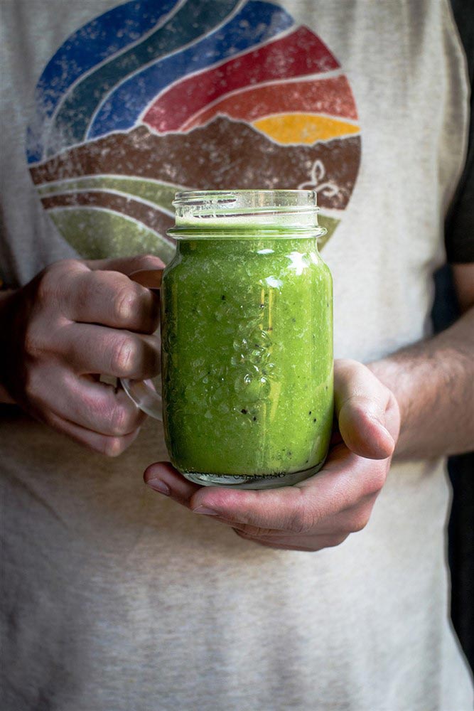 A close-up of a man holding a mason jar filled with a green smoothie
