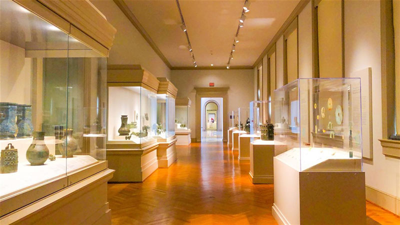 Inside a museum exhibition room with glass displays holding antiques and wooden flooring