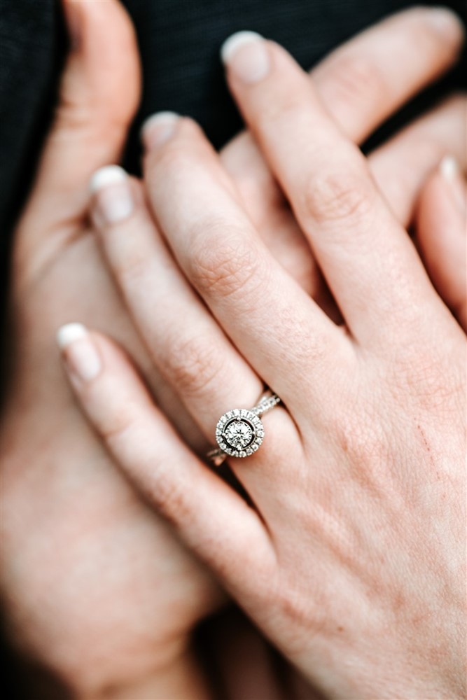 A close-up of a woman's hands resting on a man, with her diamond engagement ring in focus
