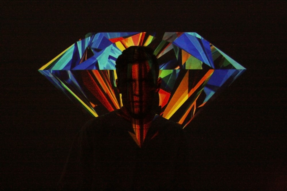 Silhouette of a person against a multicolored diamond shape on a dark background