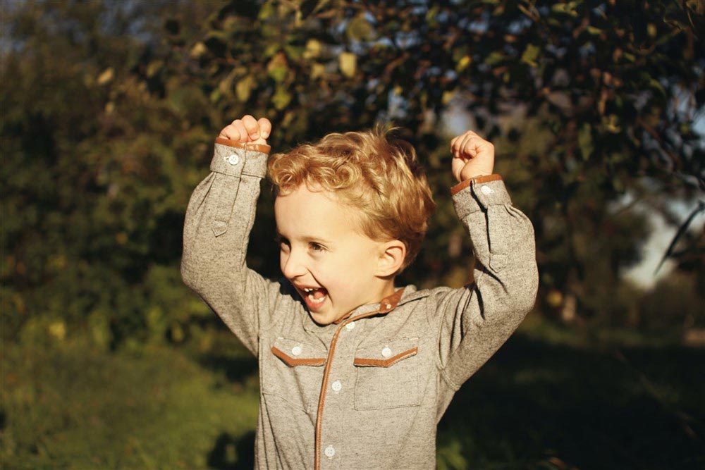 A joyful young boy with both hands raised excitedly in the air