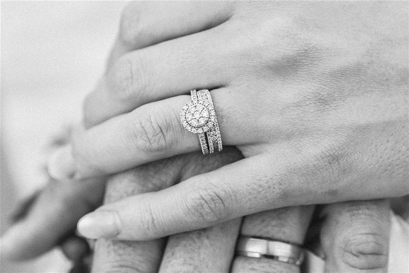 A close-up of a couple's hands placed on top of each other, with the woman's wedding ring set in focus