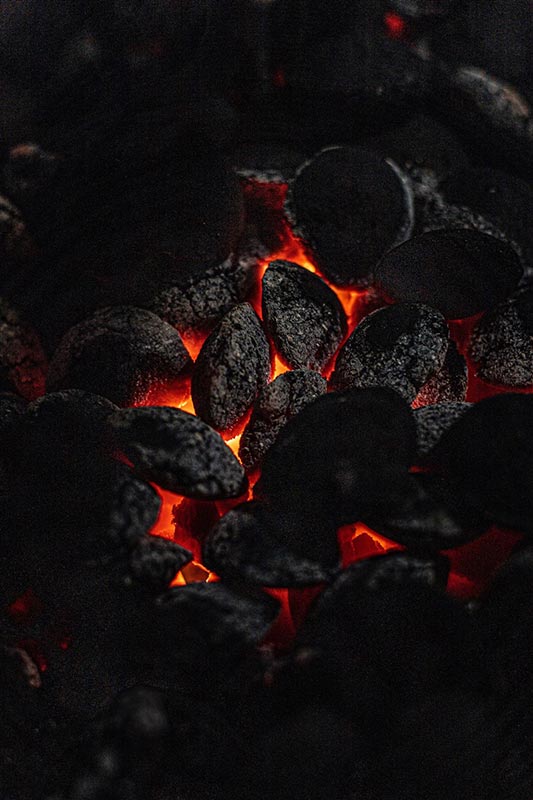Close-up of glowing charcoal in a dark environment, emitting a warm orange-red glow from beneath