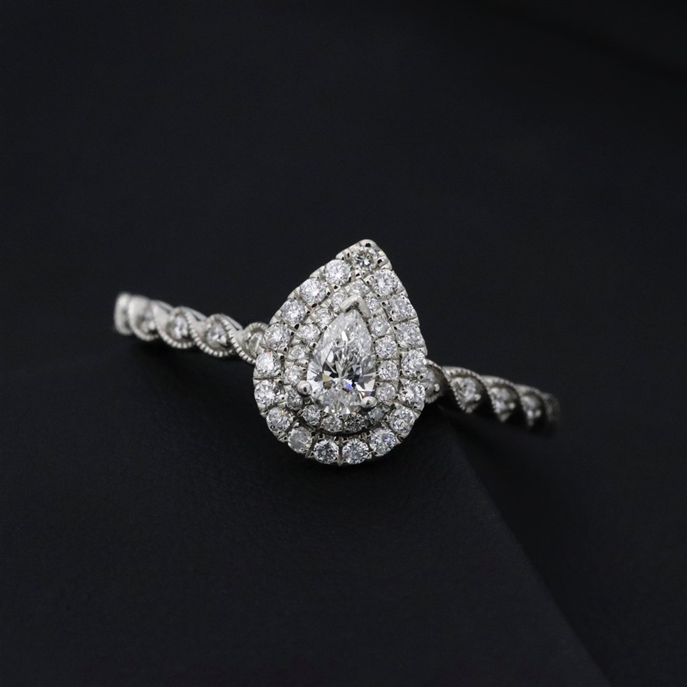 An elegant pear cut diamond ring with a double halo of smaller diamonds, set in a twisting band setting, placed aganist a black background
