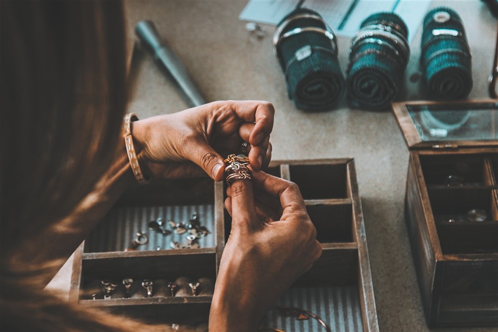 Hands delicately adjusting stackable rings one by one at a vanity table, beside a wooden jewelry box