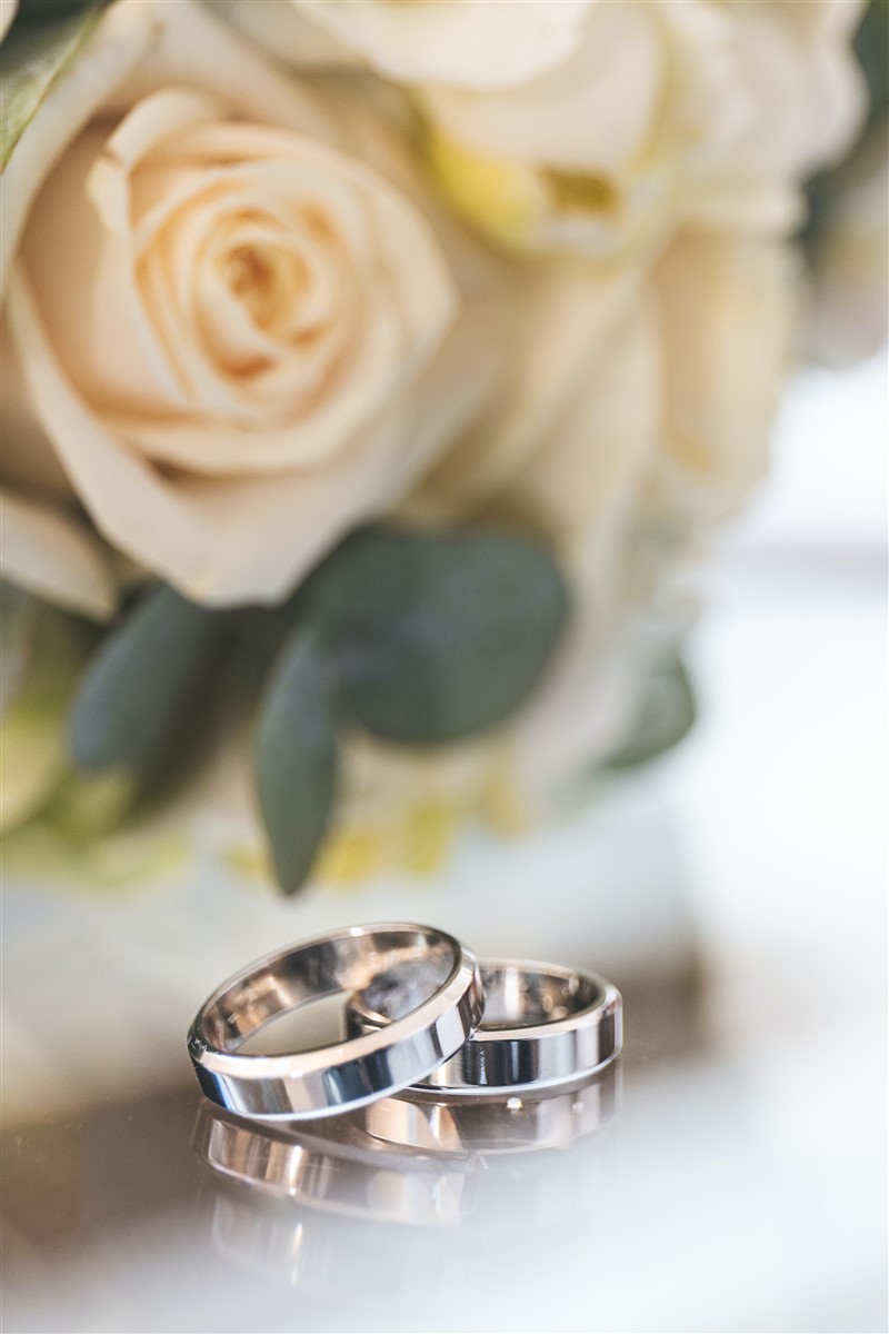 A pair of wedding rings on a table beside a bouquet of white roses
