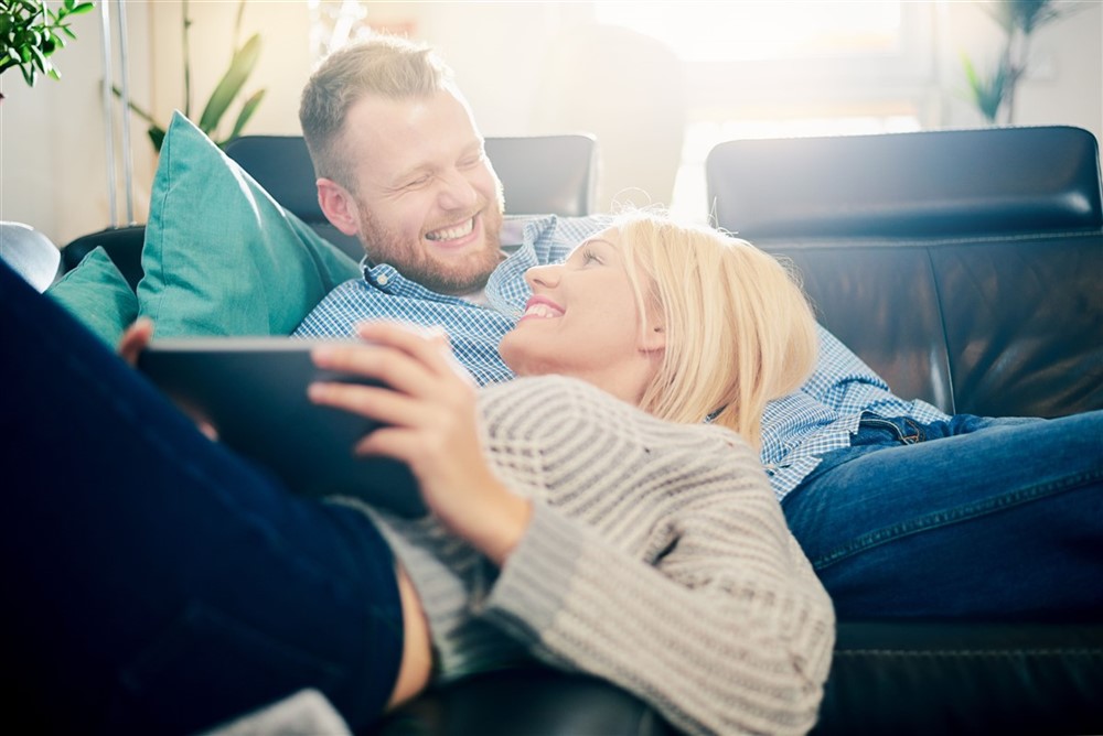 a man and woman smiling at each other on a couch