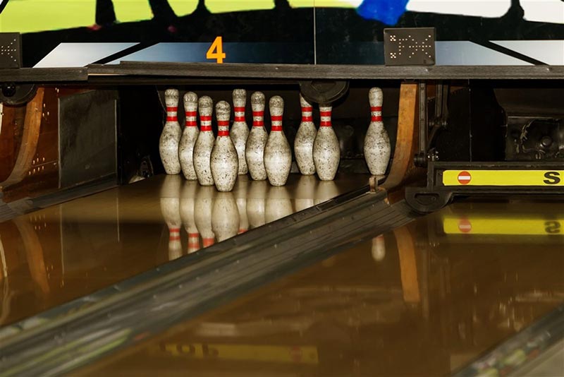 A set of ten bowling pins stands neatly arranged at the end of a wooden bowling lane