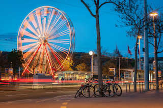 A ferris wheel illuminated by lights, towering over the city skyline at night