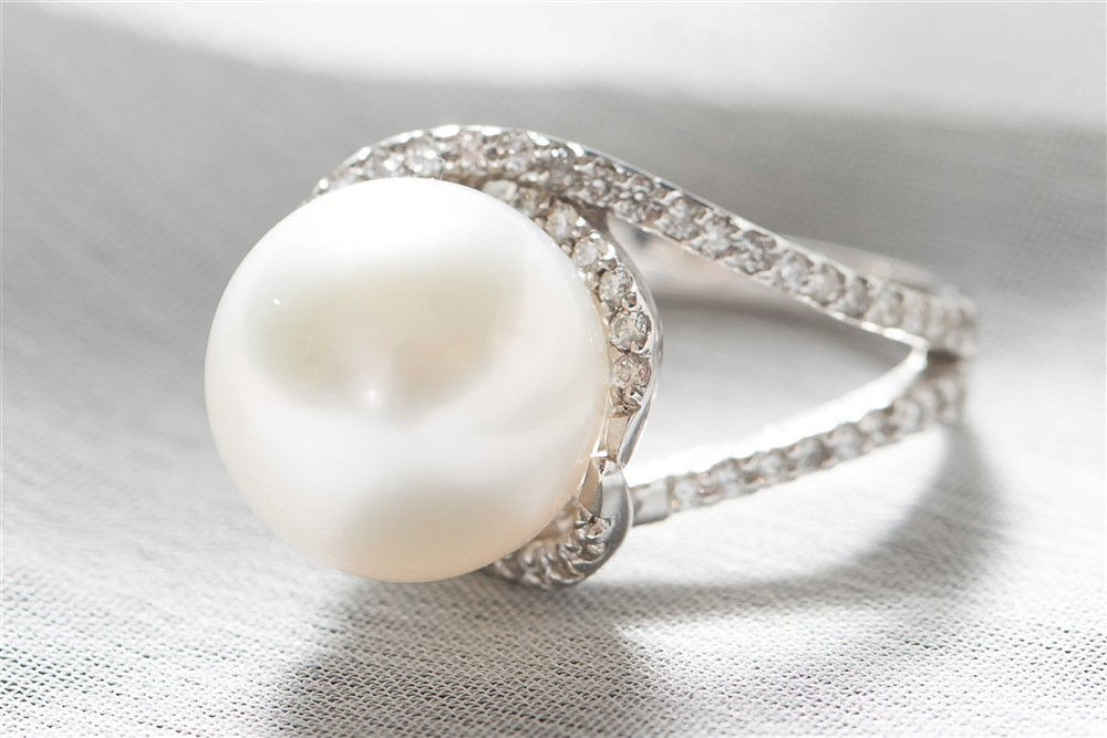 A pearl and diamond ring, set against a white surface