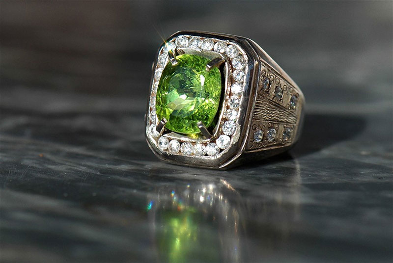 A peridot and diamond ring. displayed on a black surface
