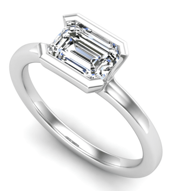 A 1/2 bezel solitaire ring shown with an emerald cut diamond in the East/West direction in white gold