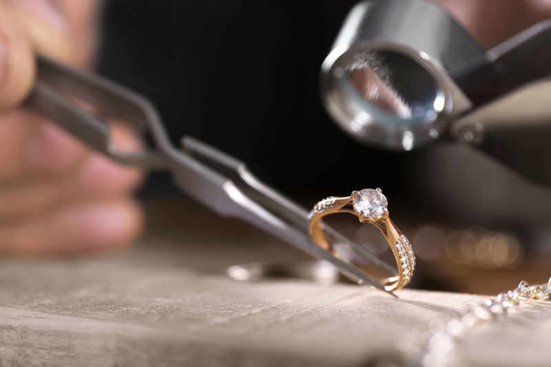 A close-up of a diamond ring being examined with a jeweler's loupe and tweezers
